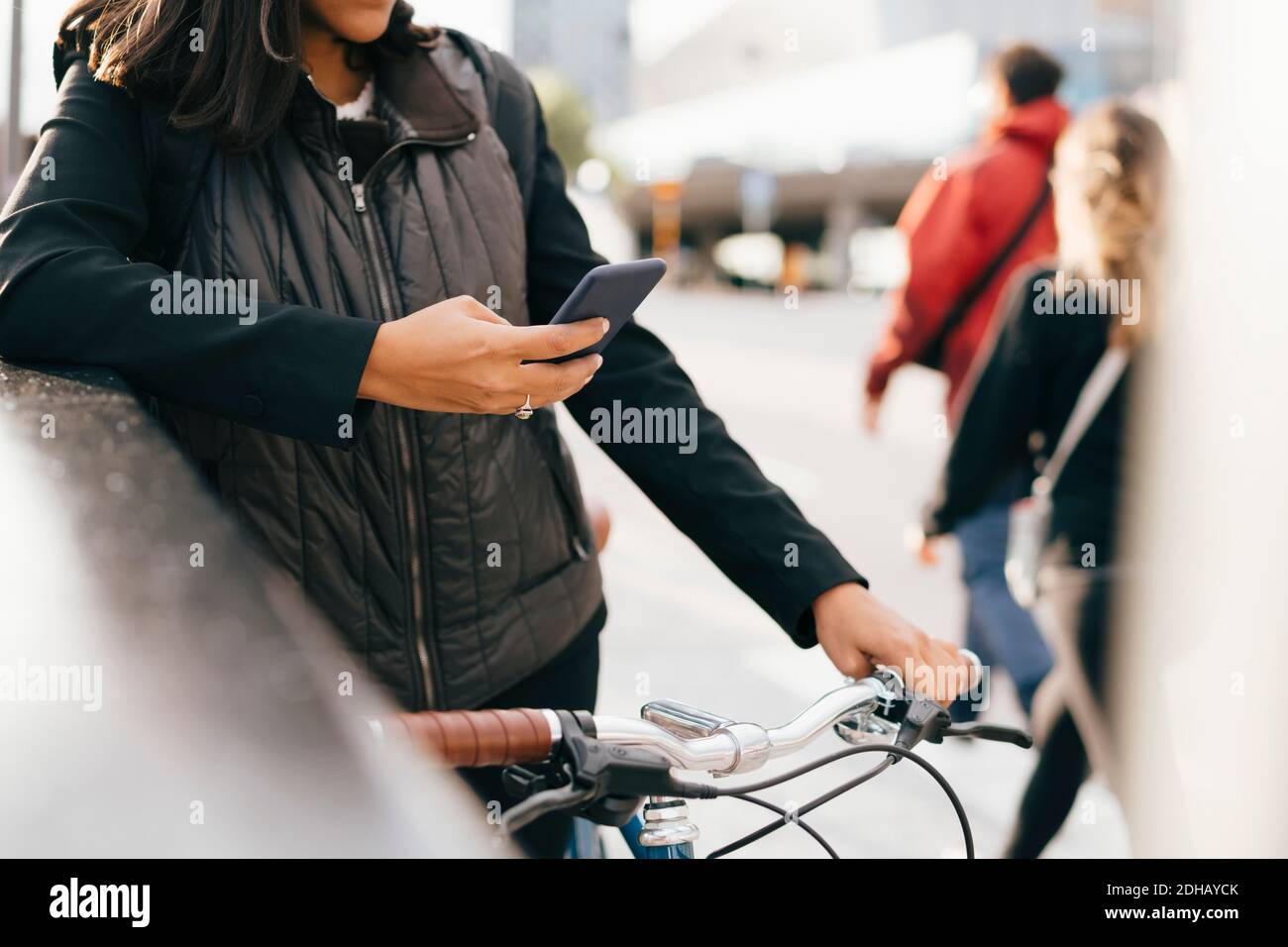 Midsection of businesswoman using smart phone while standing with bicycle in city Stock Photo