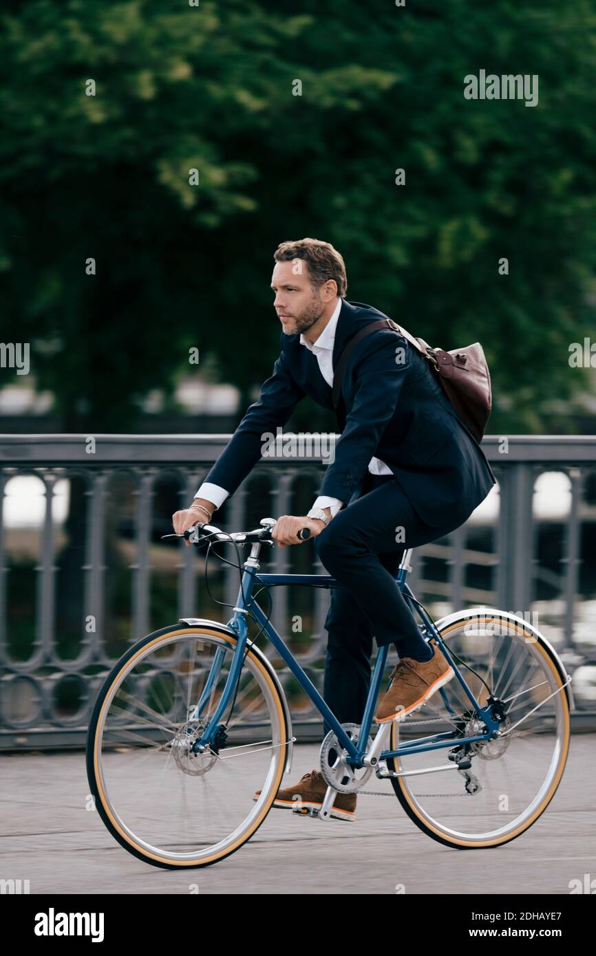 Full length of confident businessman riding bicycle on road in city Stock Photo