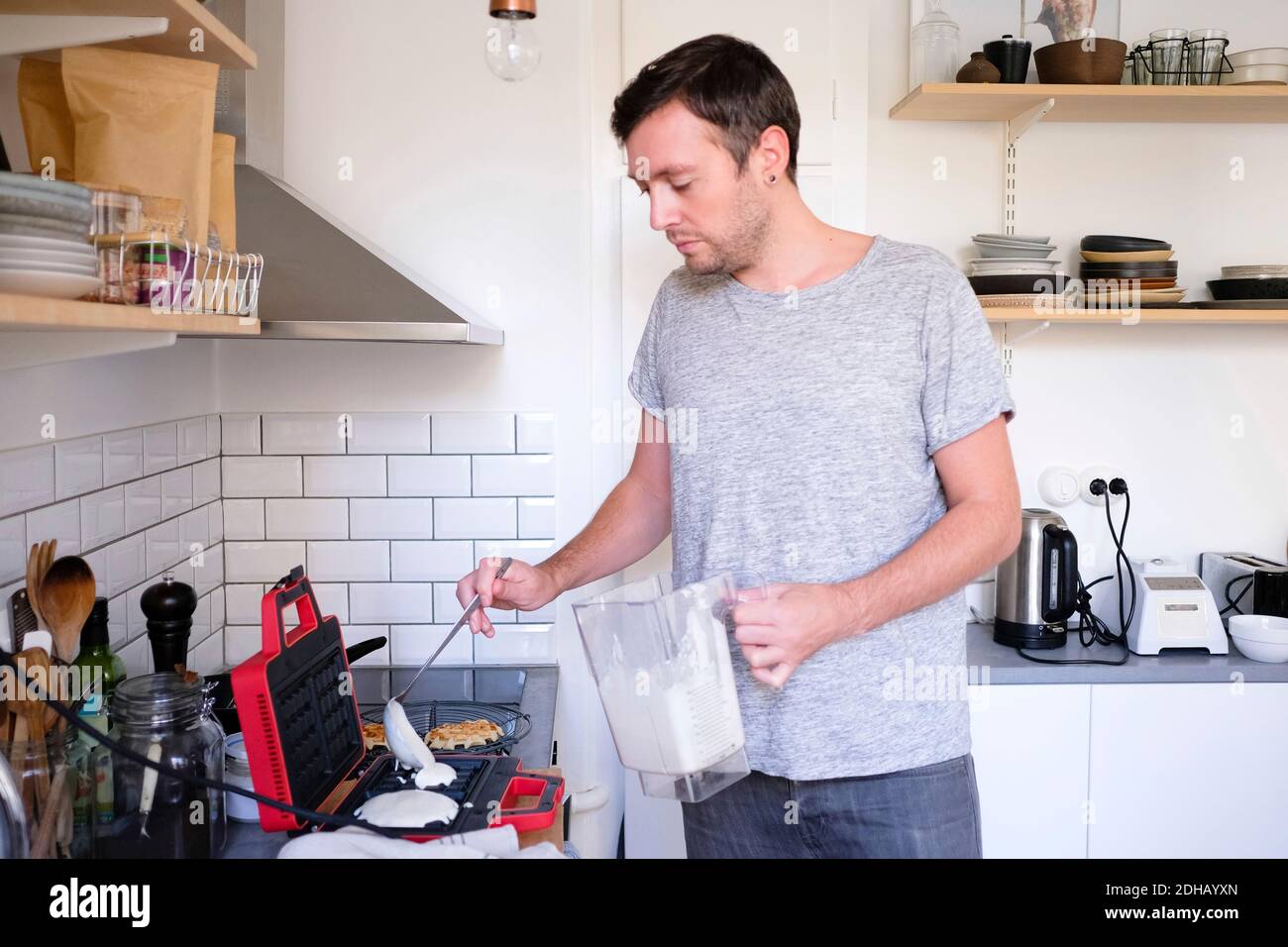 Man pouring batter on waffle iron at kitchen counter Stock Photo