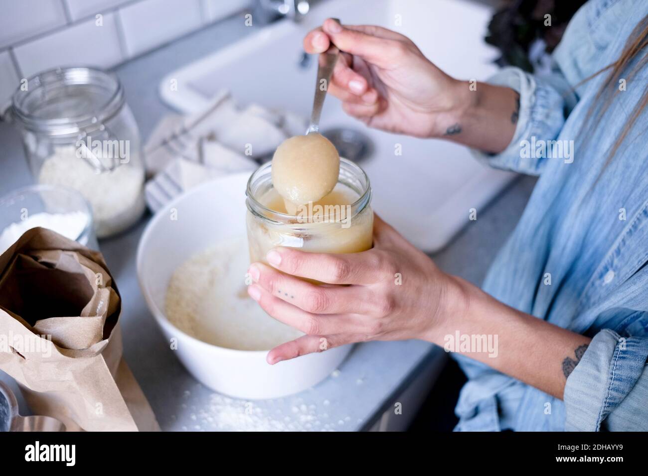 Midsection of woman adding ingredient in bowl at kitchen counter Stock Photo