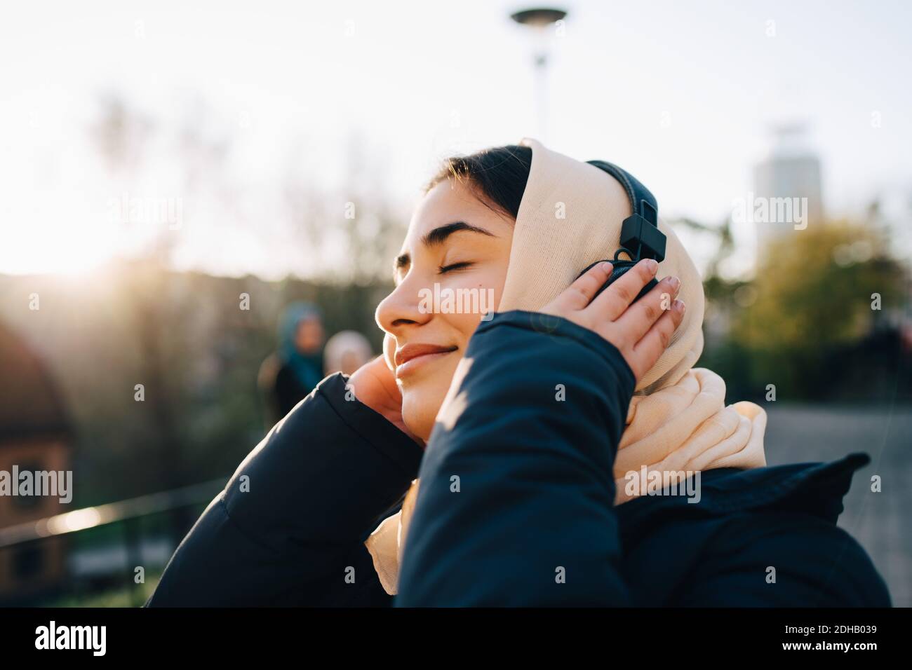Teenage girl listening to headphones with eyes closed against sky Stock Photo