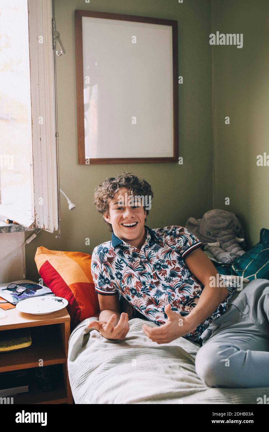 Portrait of cheerful teenage boy leaning on bed at home Stock Photo