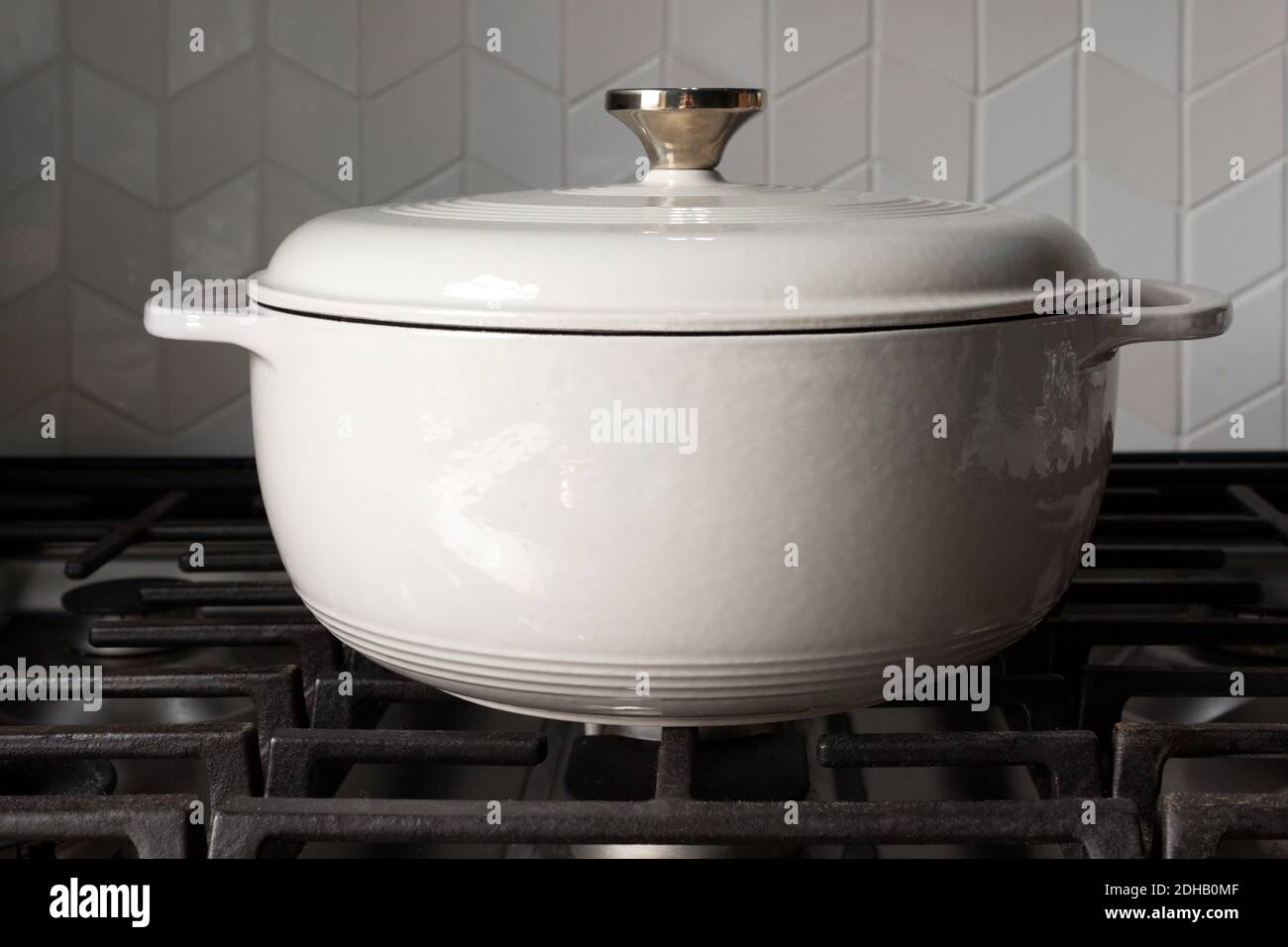 a large, white enameled cast iron crock pot on an unlit stove top with natural lighting and a chevron backsplash Stock Photo