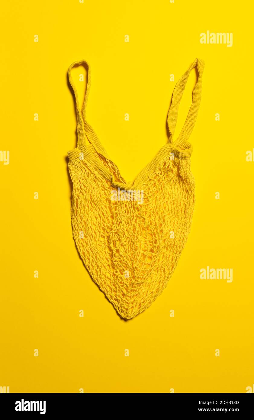 One empty yellow mesh bag on bright yellow paper background. Flat lay. Vertical orientation. Conscious consumerism and eco friendly shopping concept. Stock Photo