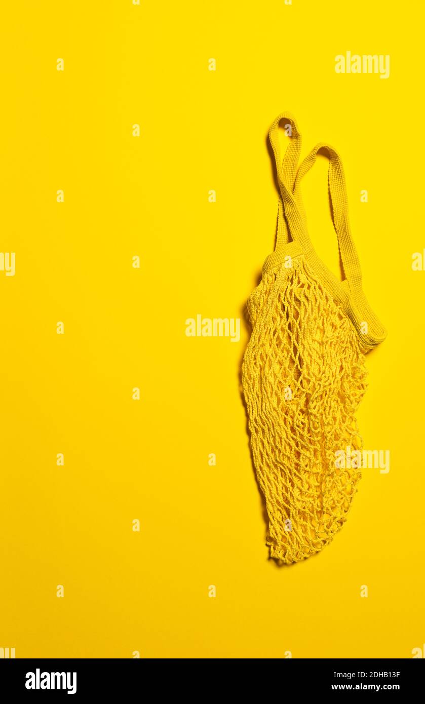 Empty yellow mesh bag on bright yellow paper background. Flat lay. Vertical orientation. Conscious consumerism and eco friendly shopping concept. Copy Stock Photo