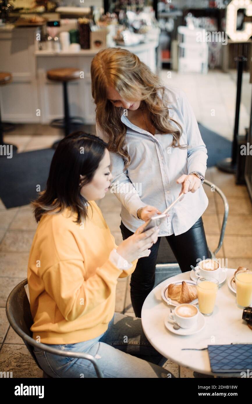 Multi-ethnic female photographers sharing smart phone at cafe Stock Photo