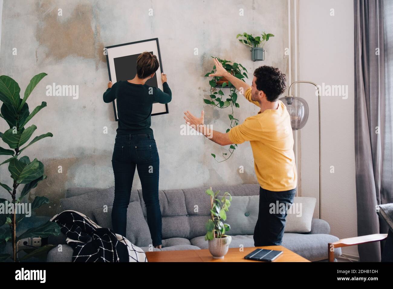 Mid adult man guiding girlfriend in hanging picture frame on wall at