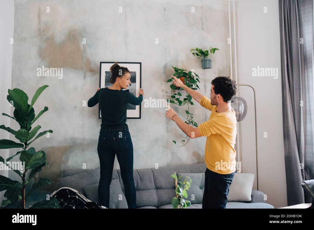 Boyfriend guiding girlfriend in hanging picture frame on wall at new
