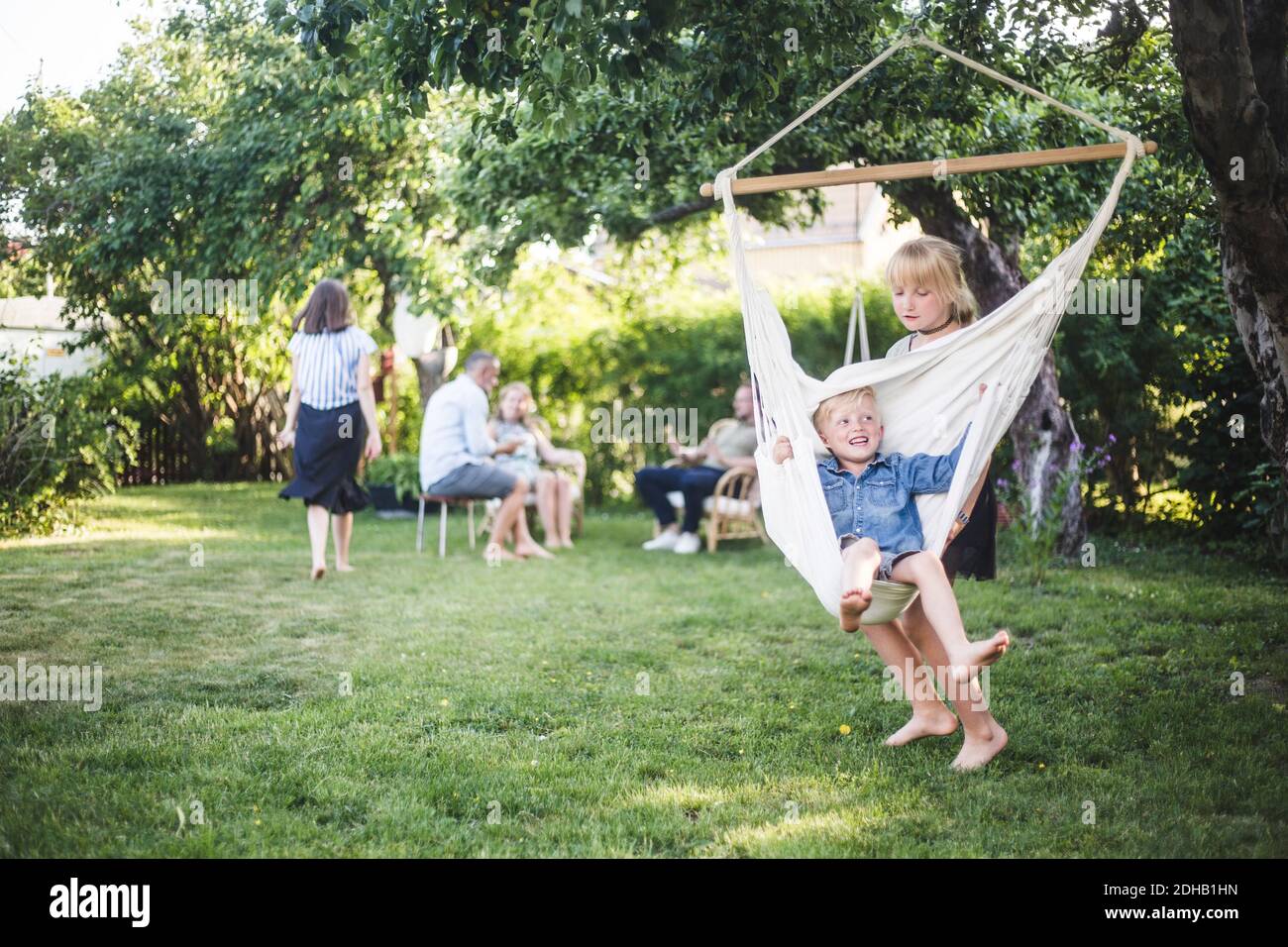 Sister pushing happy boy on swing in backyard Stock Photo