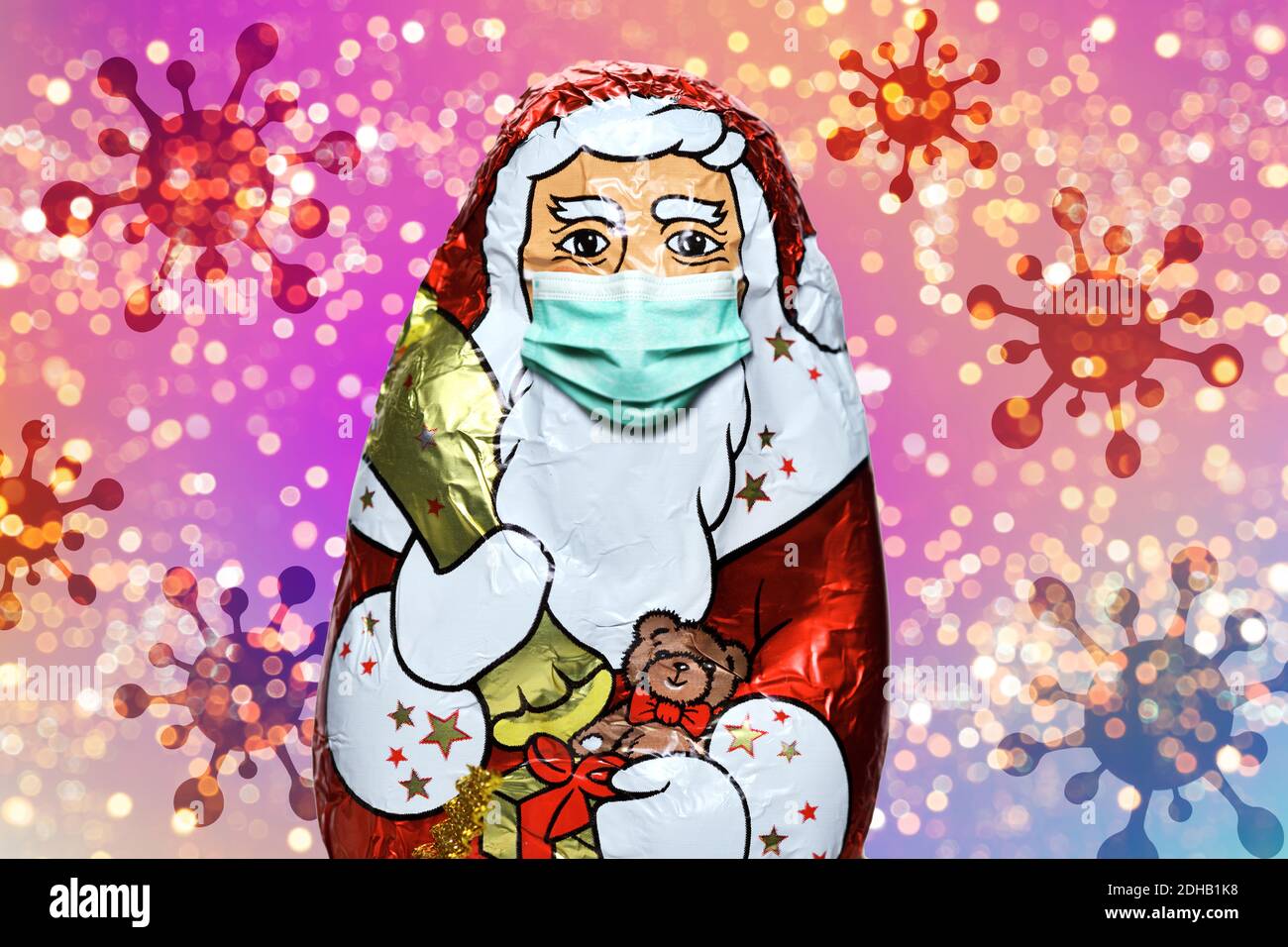 FOTOMONTAGE, Schoko-Weihnachtsmann mit Schutzmaske und Coronaviren, Weihnachtsfest zu Corona-Zeiten und Corona-Beschränkungen Stock Photo