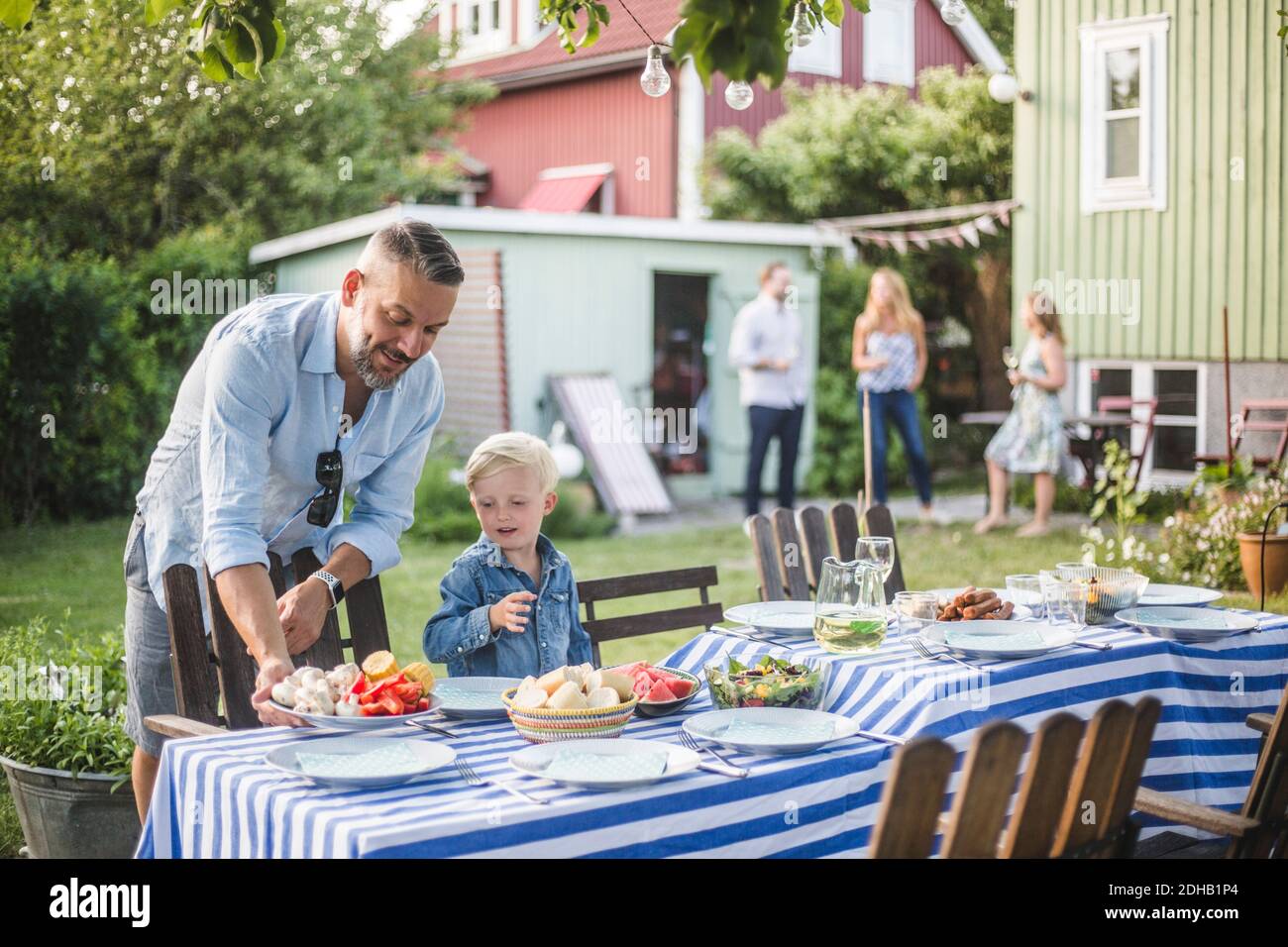 Father talking to son while arranging food plate on table in backyard Stock Photo