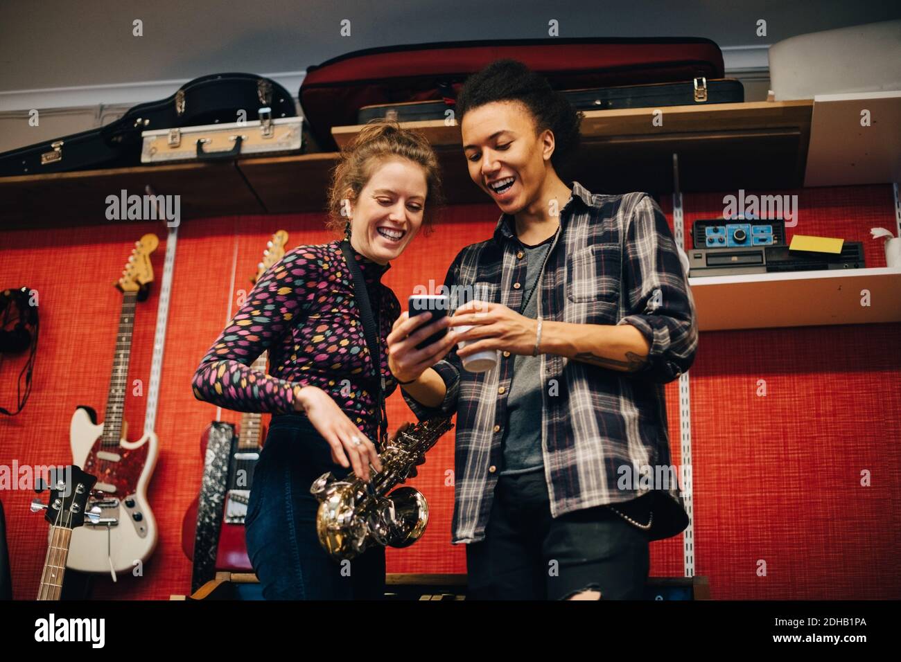 Woman with saxophone looking at man using smart phone while practicing at recording studio Stock Photo
