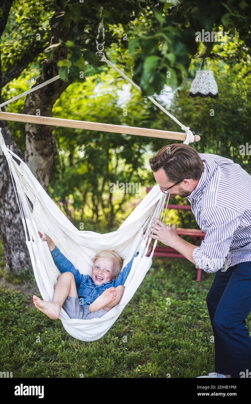Mature father swinging son in backyard during weekend Stock Photo