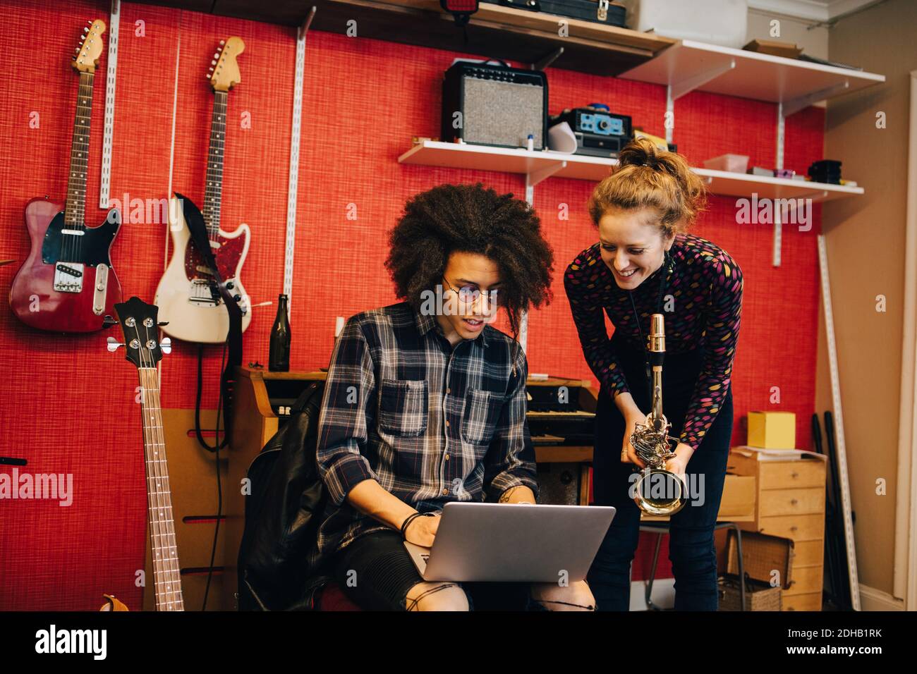 Woman with saxophone looking at man using laptop while practicing at recording studio Stock Photo