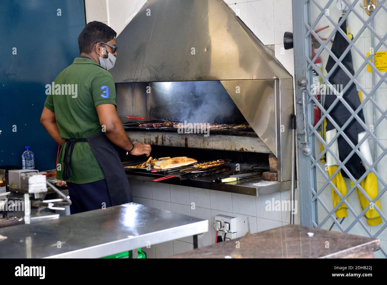 Chef toasting pitta bread and cooking meat over charcoal grill with fume hood above in restaurant Stock Photo