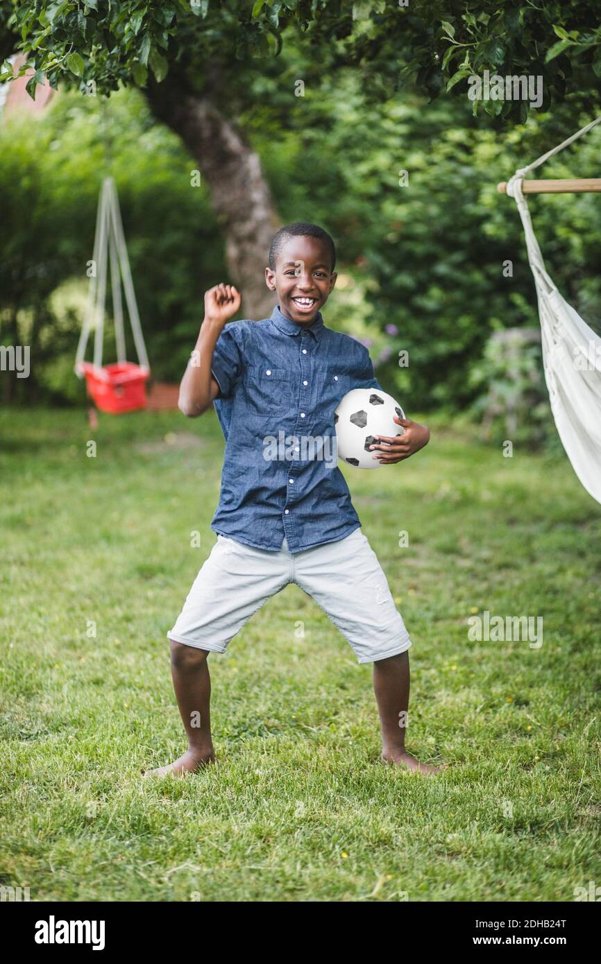 Full length of smiling boy dancing while holding soccer ball at backyard Stock Photo