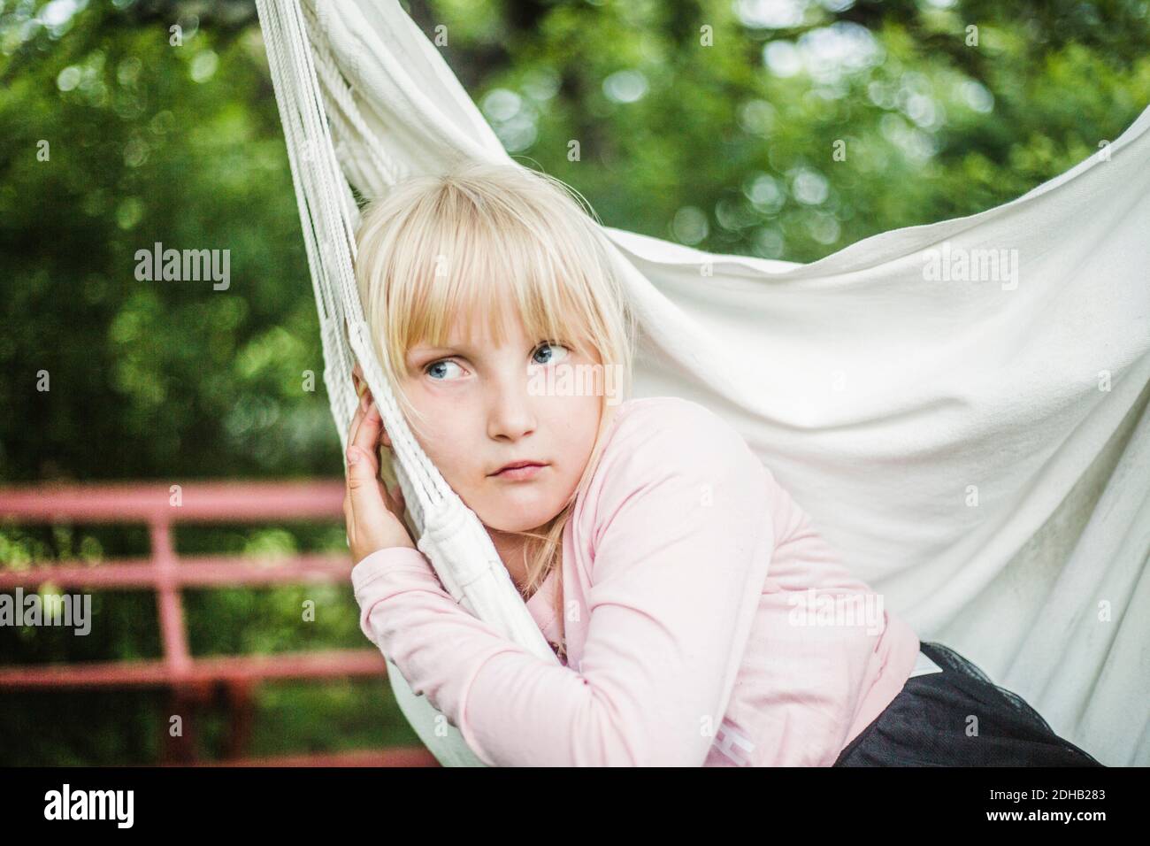Thoughtful girl looking away while sitting on white swing in garden Stock Photo