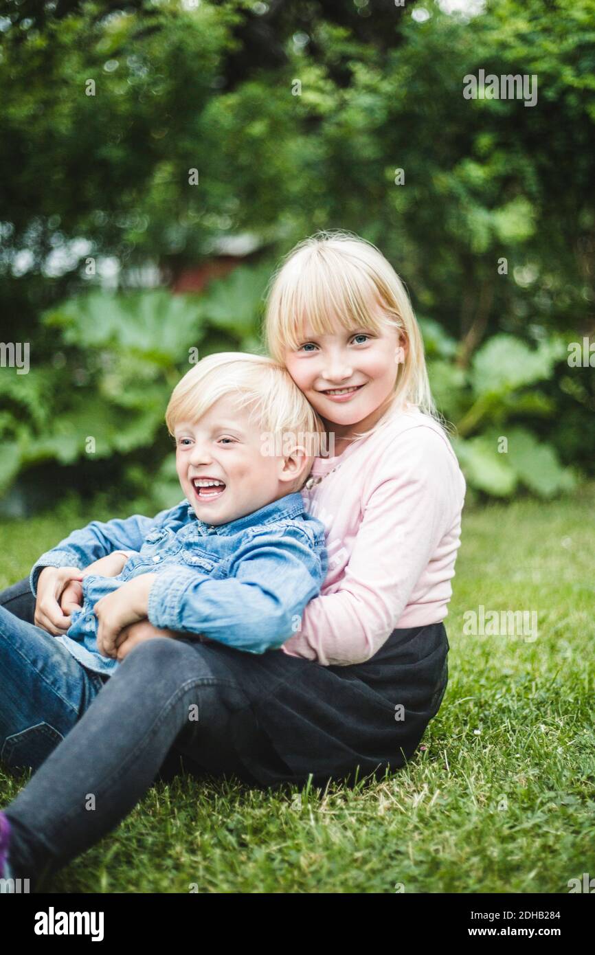Happy brother and sister sitting together on grassy field Stock Photo ...