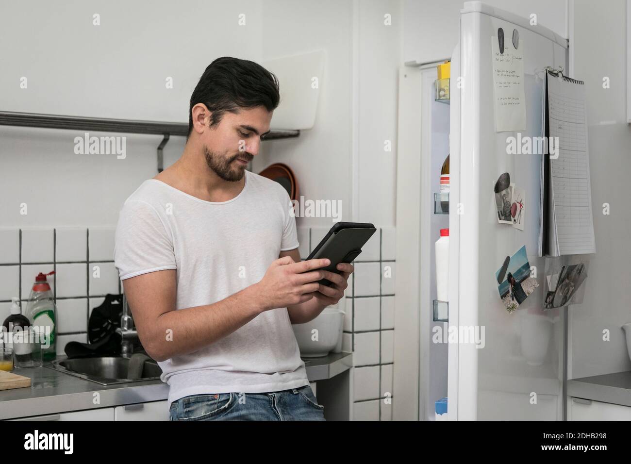 Young man using digital tablet while standing by open refrigerator at kitchen Stock Photo