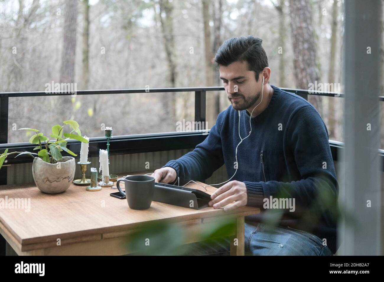 Man with headphones using digital tablet while sitting at table in balcony Stock Photo