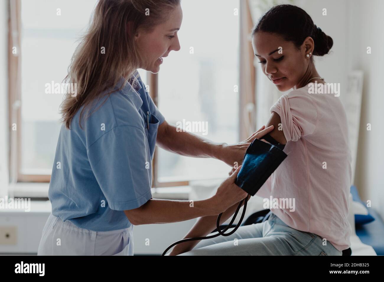 Mature nurse checking patient's blood pressure in examination room at clinic Stock Photo