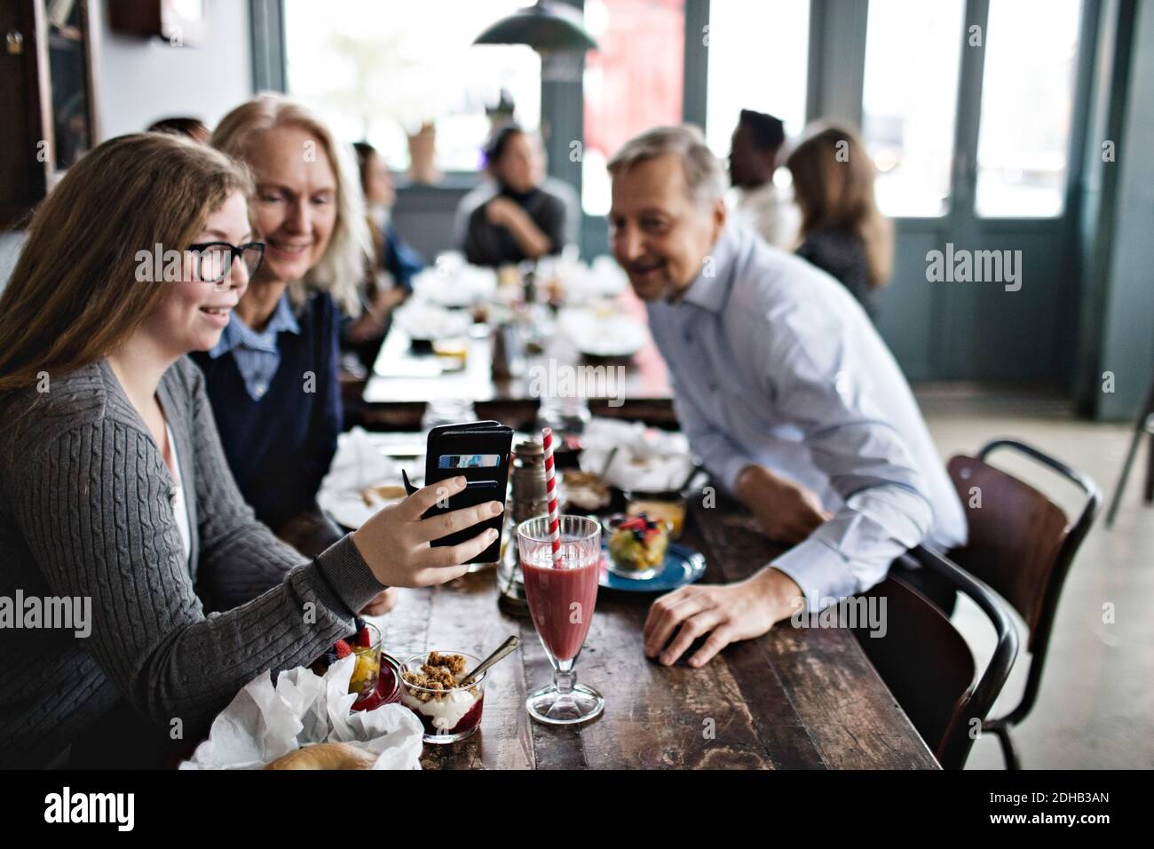 Smiling daughter taking selfie with parents while sitting at table in restaurant Stock Photo