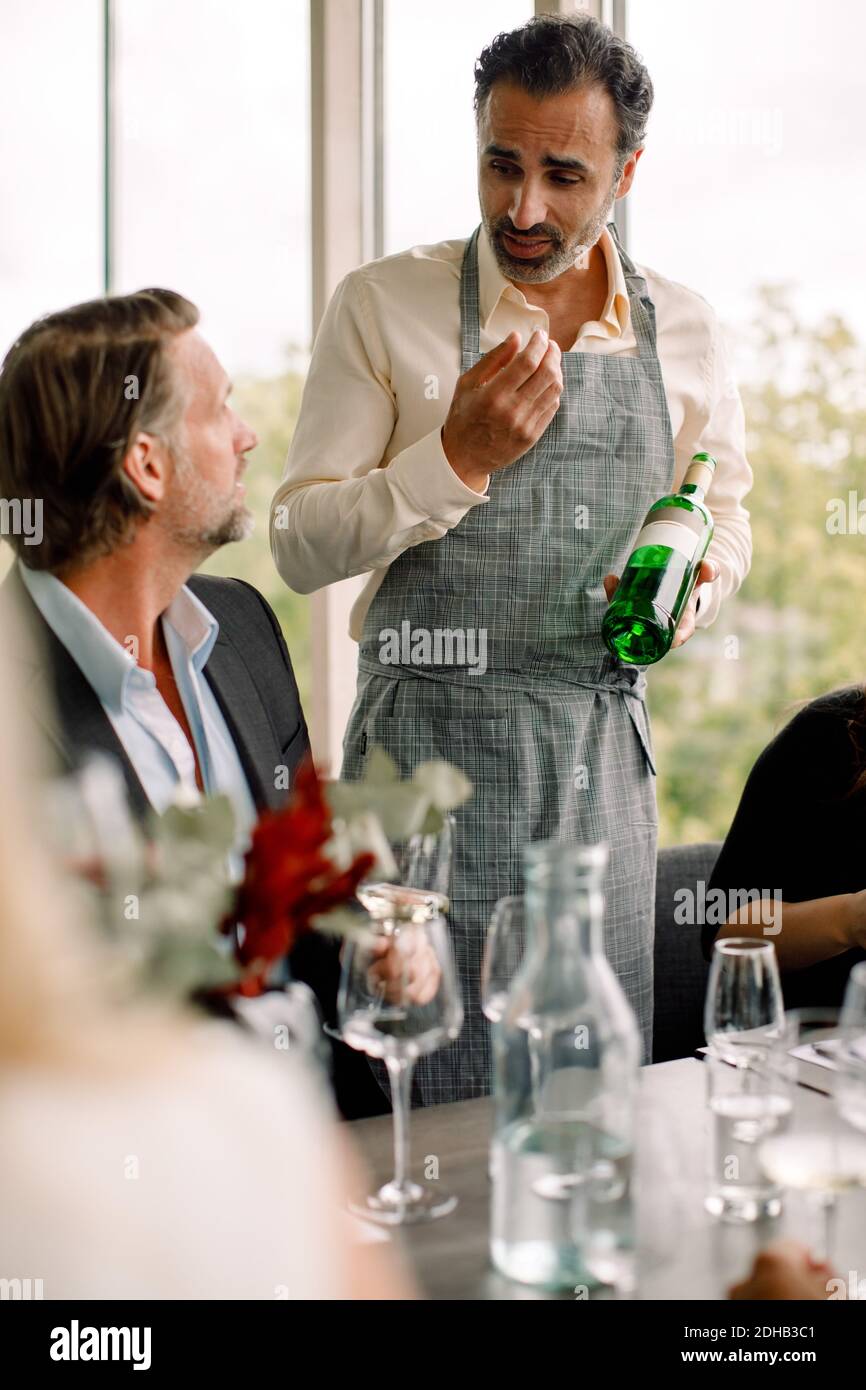 Businessman discussing with male colleague while holding wine bottle at convention center Stock Photo