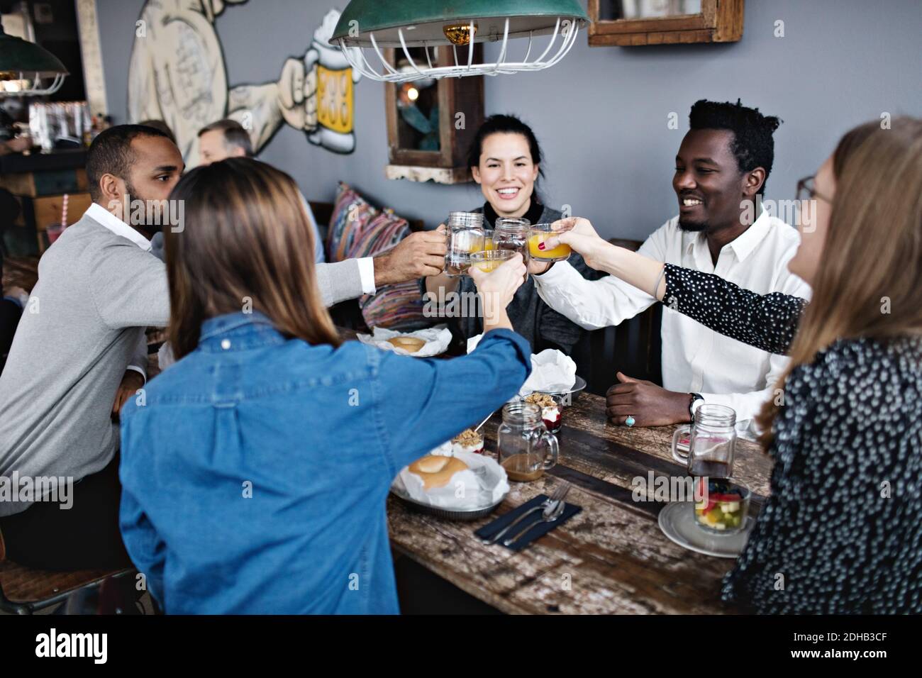 Happy friends toasting drink while sitting at dining table in restaurant Stock Photo