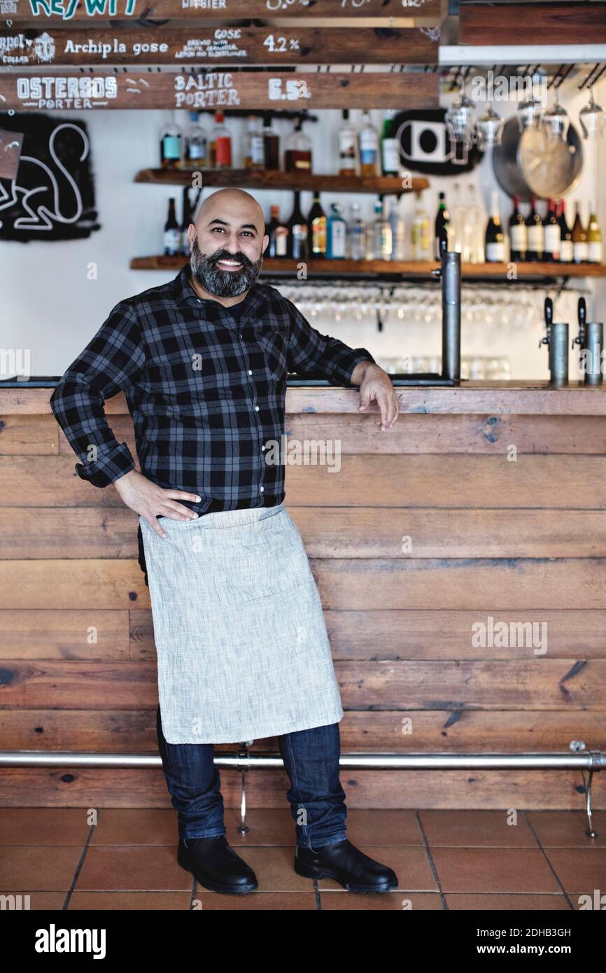 Full length of confident bartender standing by bar counter Stock Photo