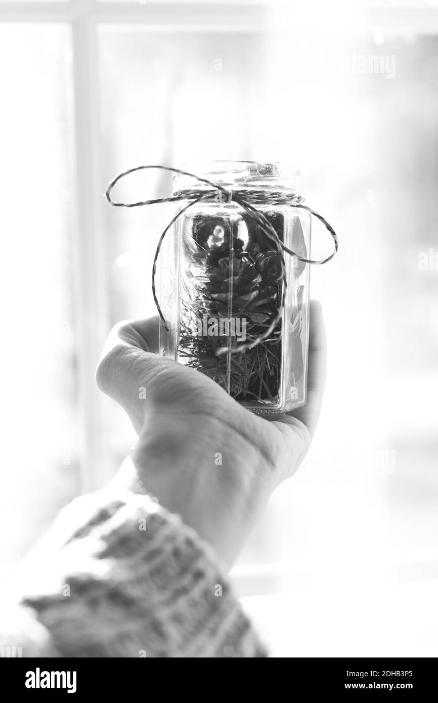 Hand holding Christmas decorations in a jar with ribbon in front of a window Stock Photo