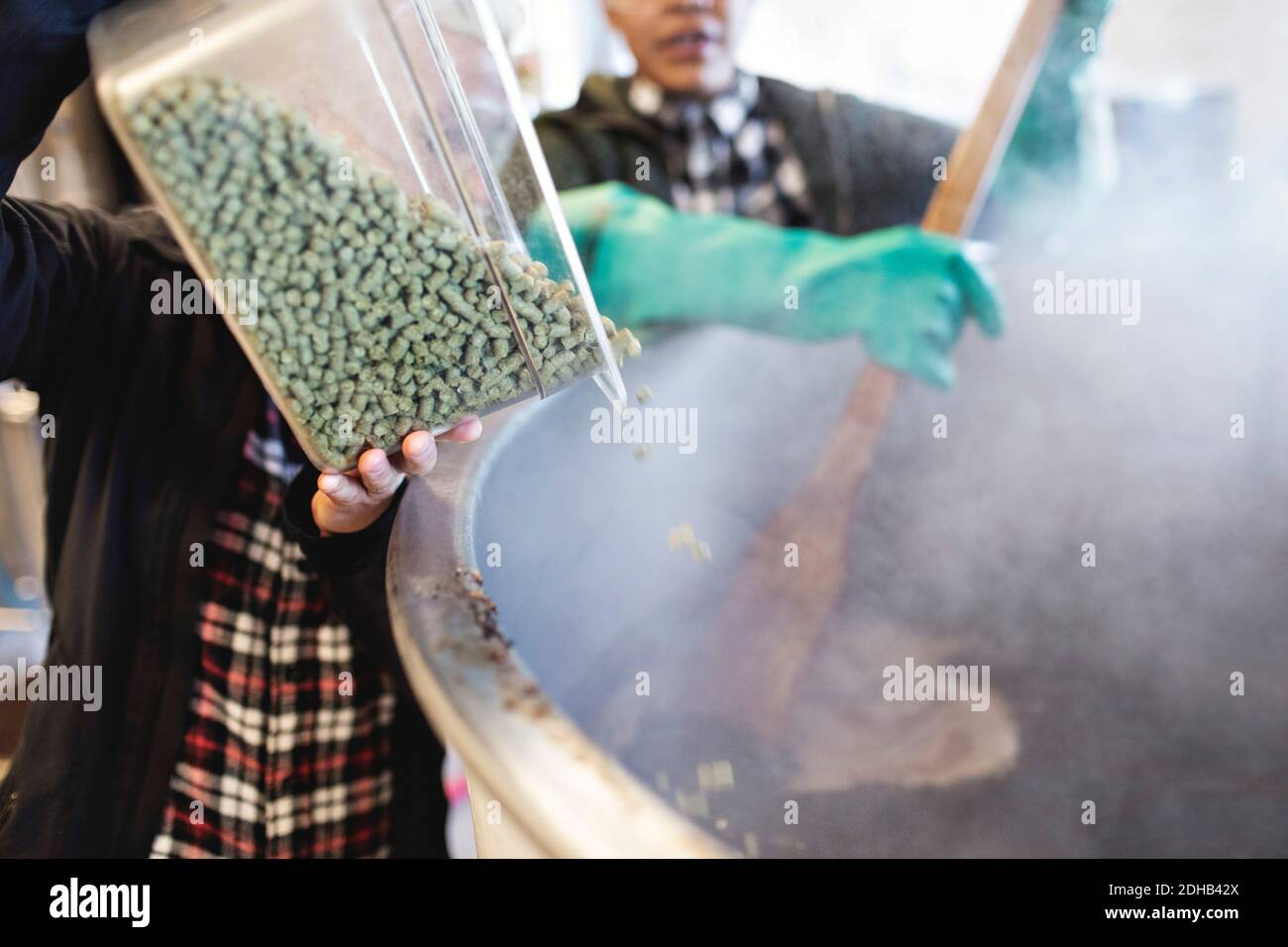 Woman pouring ingredients in container while assisting coworker at brewery Stock Photo