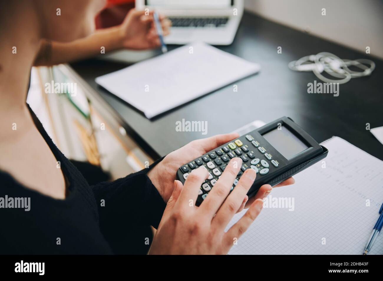 Midsection of young female student using calculator in classroom at