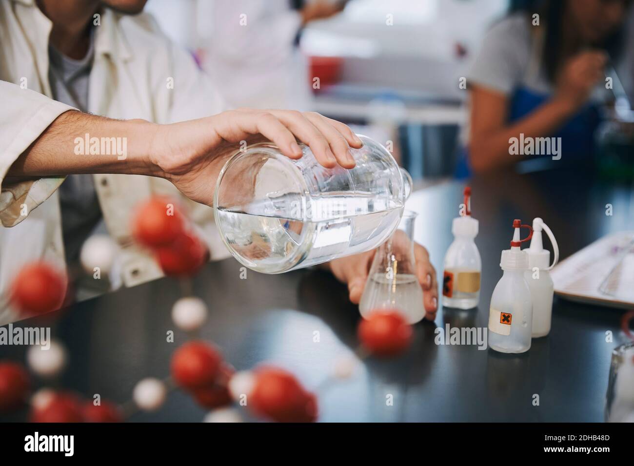 Midsection of young male student pouring liquid solution in flask on table at laboratory Stock Photo