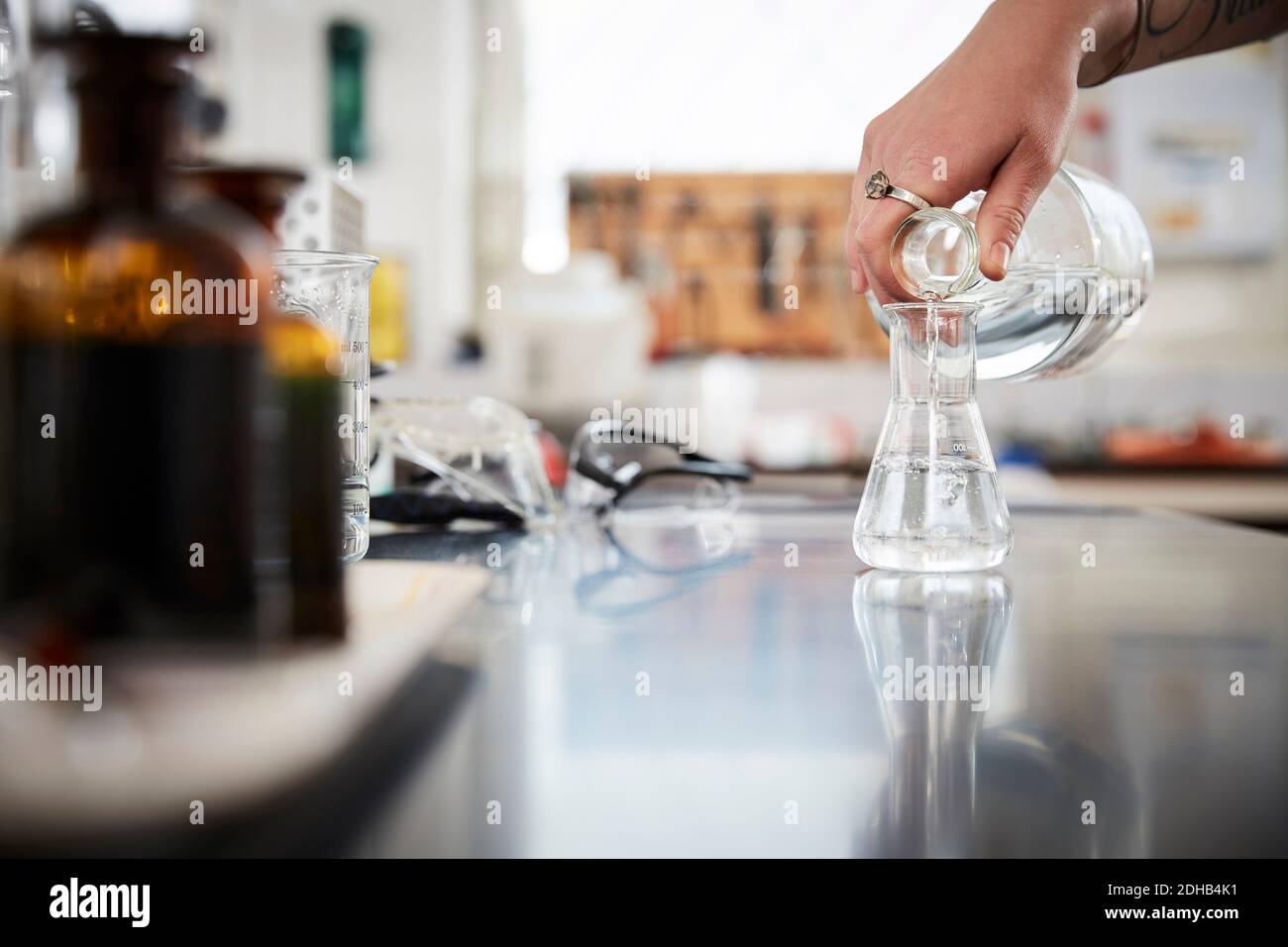 Cropped hand of female student pouring liquid solution in flask from bottle at laboratory Stock Photo