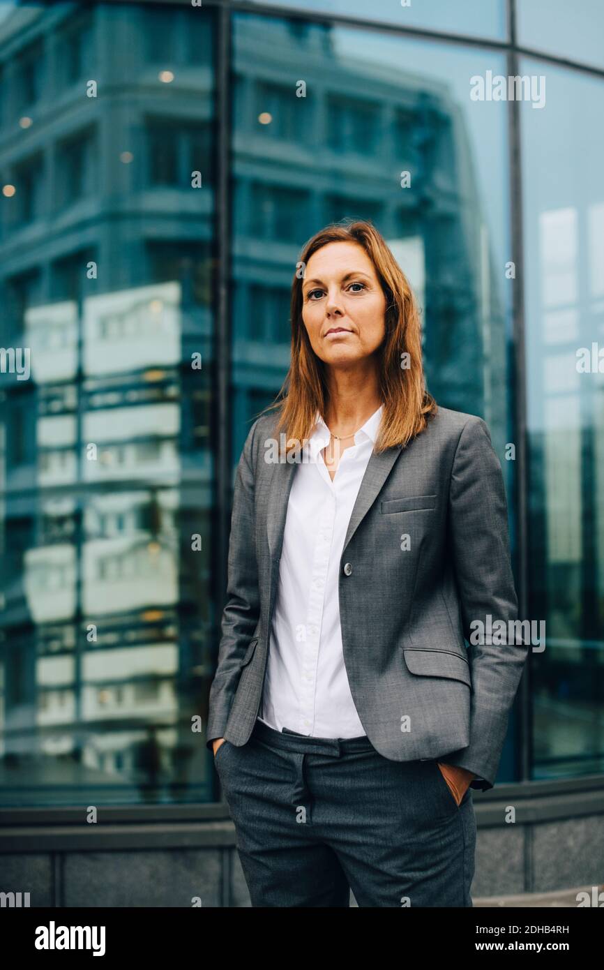 Portrait of confident businesswoman standing against reflection on glass building Stock Photo