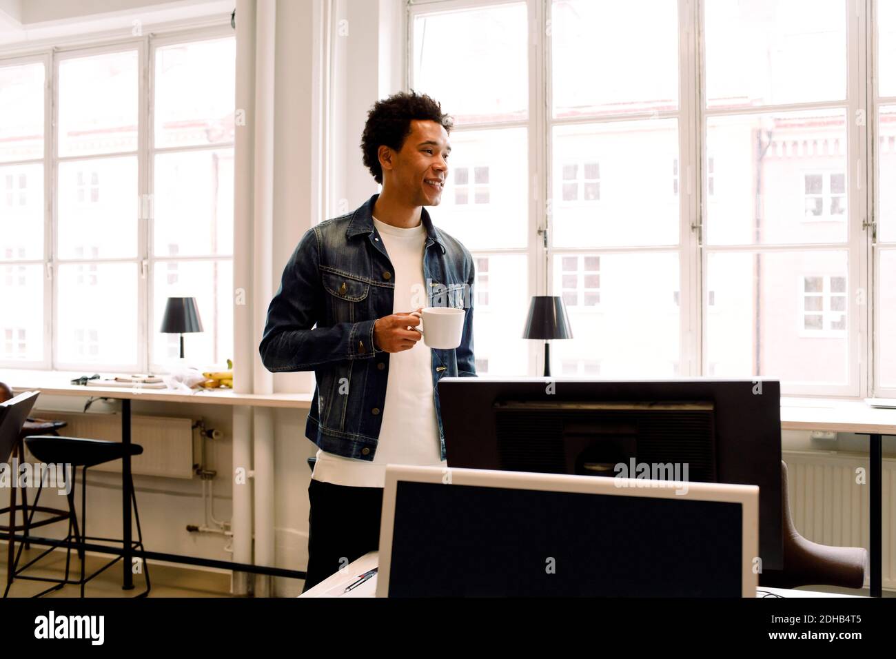 Male executive holding cup while looking away in office Stock Photo