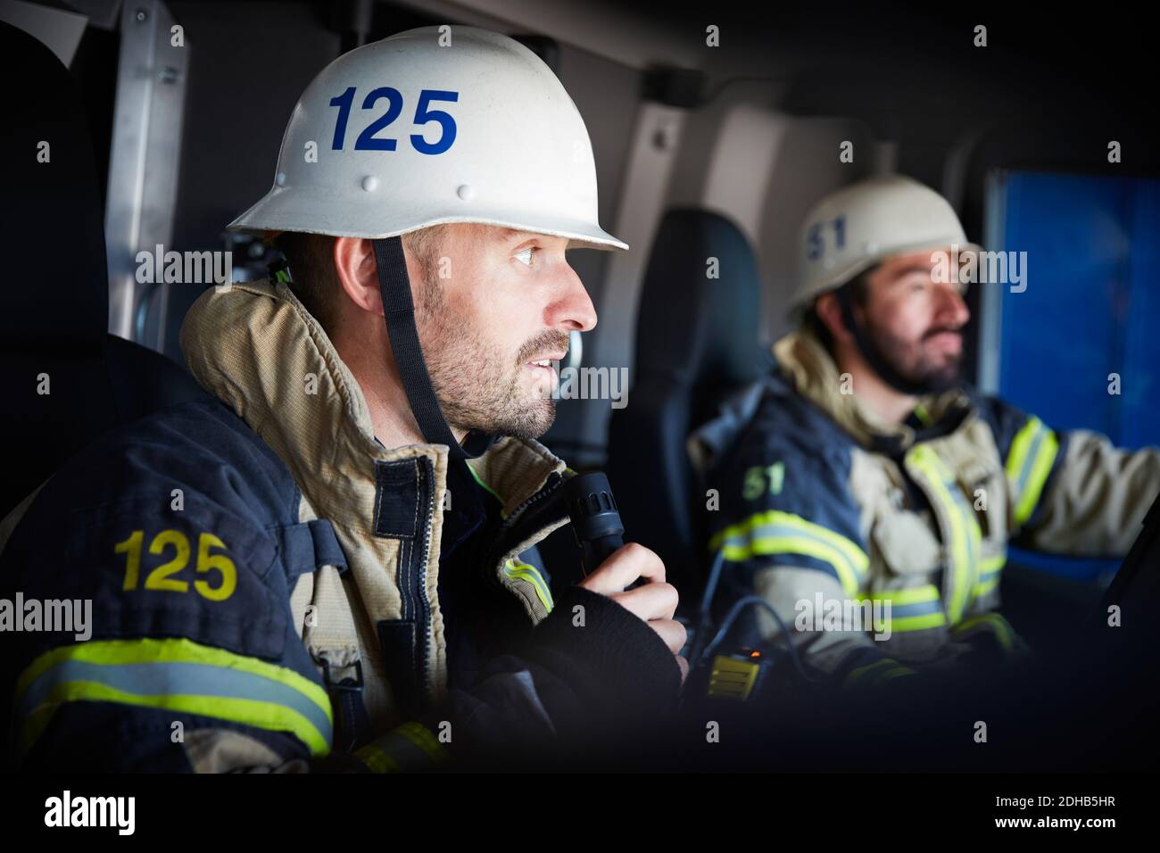 Firefighter talking on microphone while sitting with coworker in fire engine Stock Photo