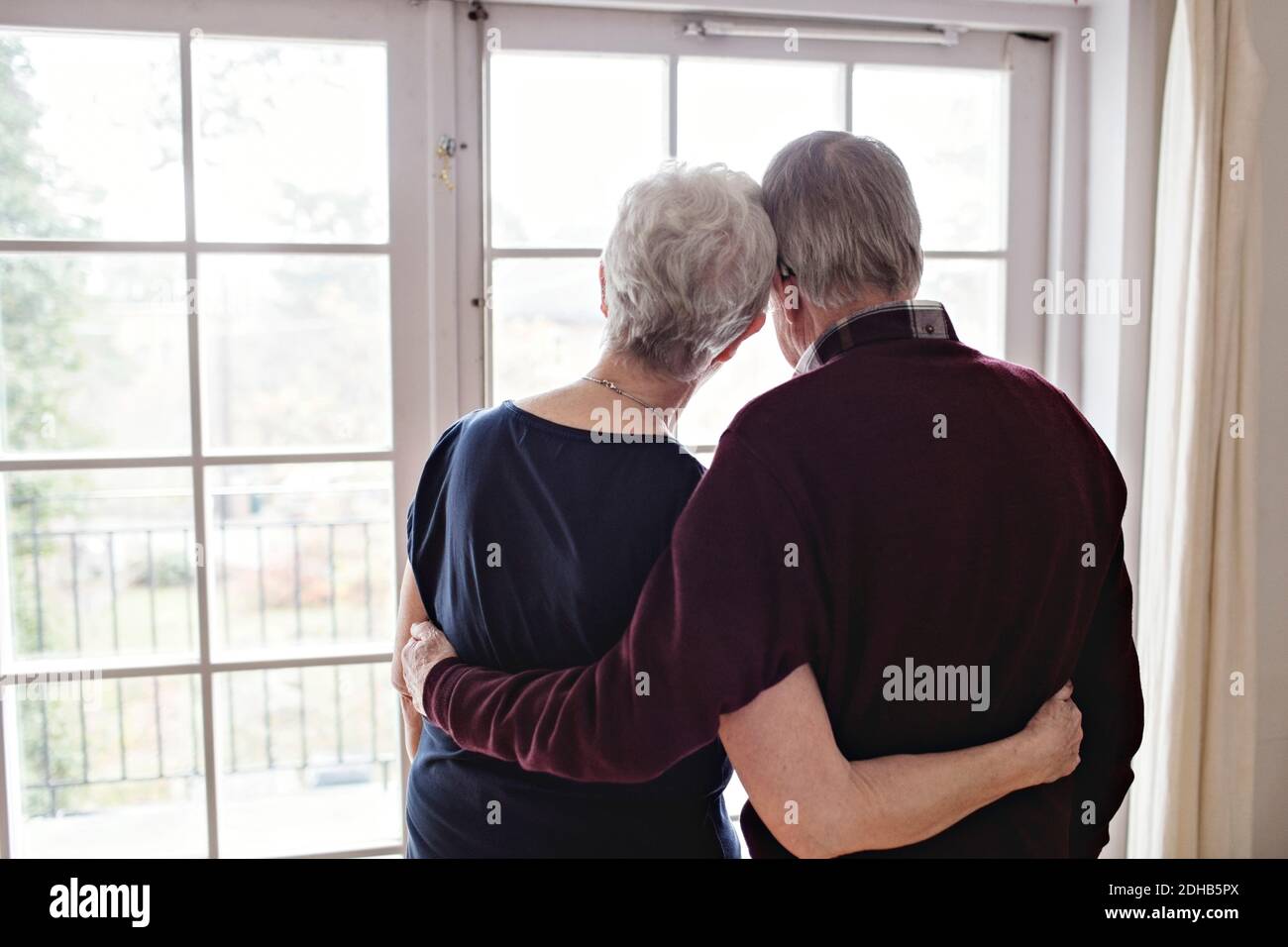 Rear view of retired couple looking through window at home Stock Photo
