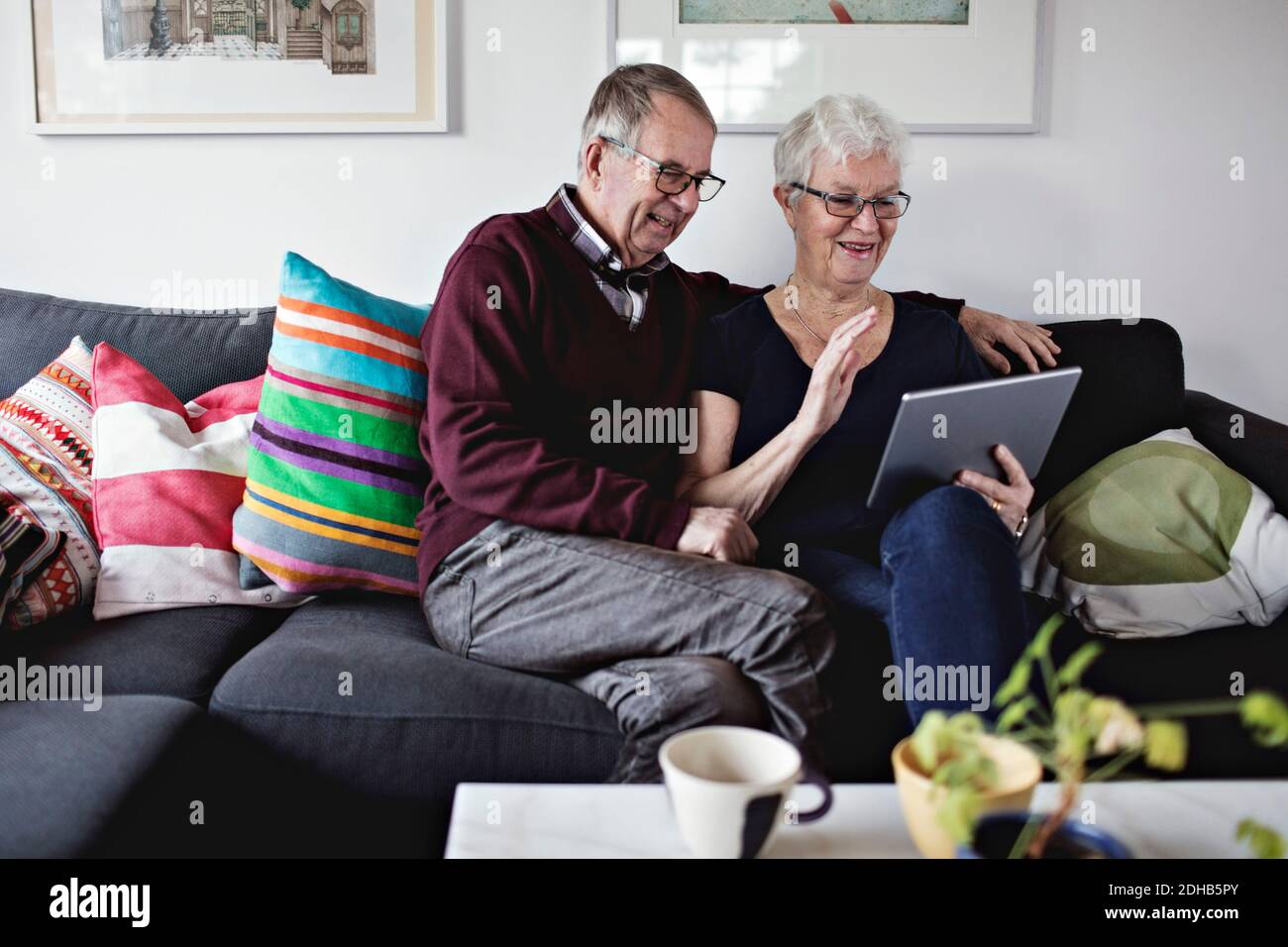 Smiling senior couple sitting on sofa sharing digital tablet in living room at home Stock Photo