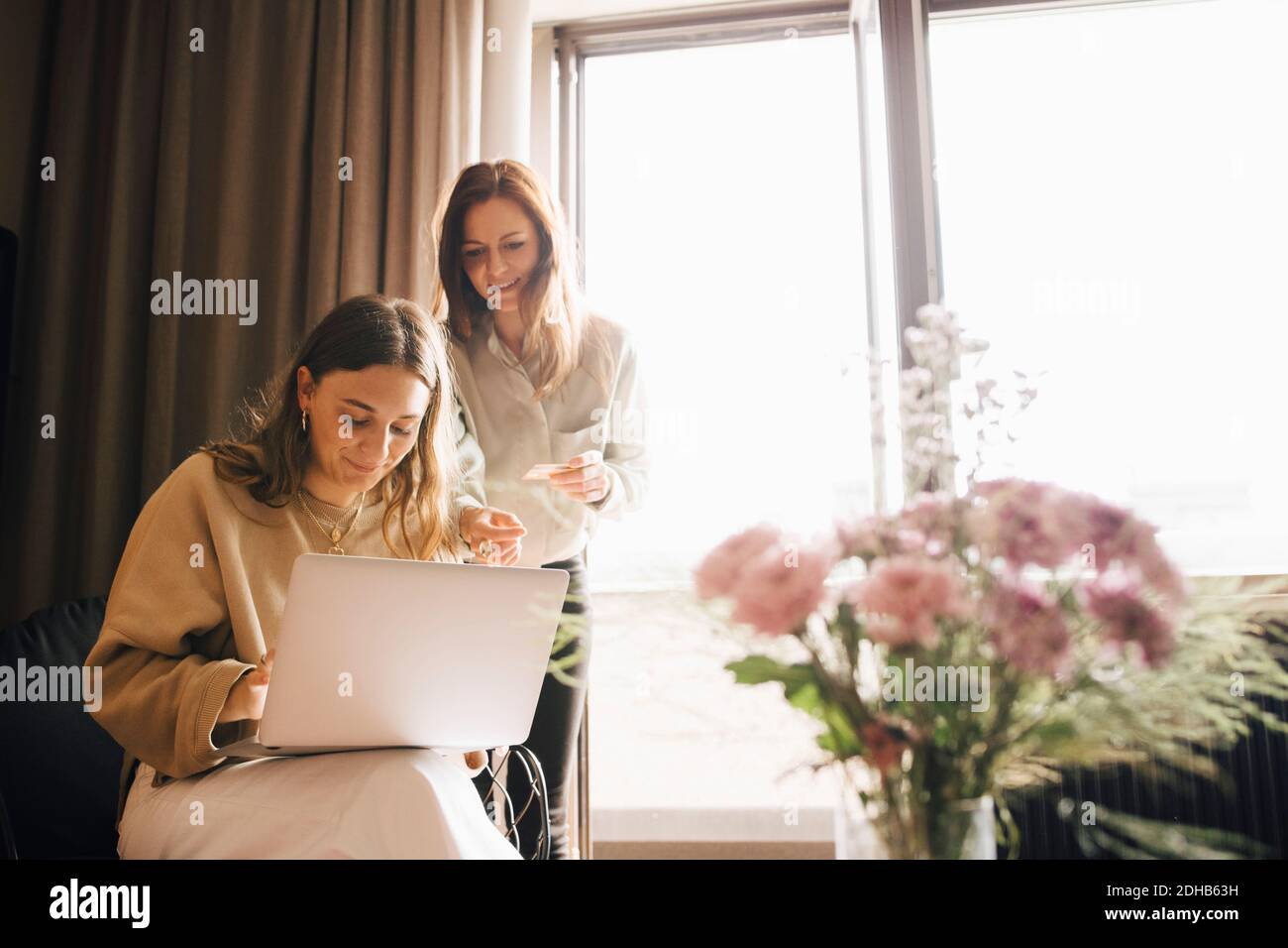 Smiling friends shopping online with credit card through laptop in hotel room Stock Photo