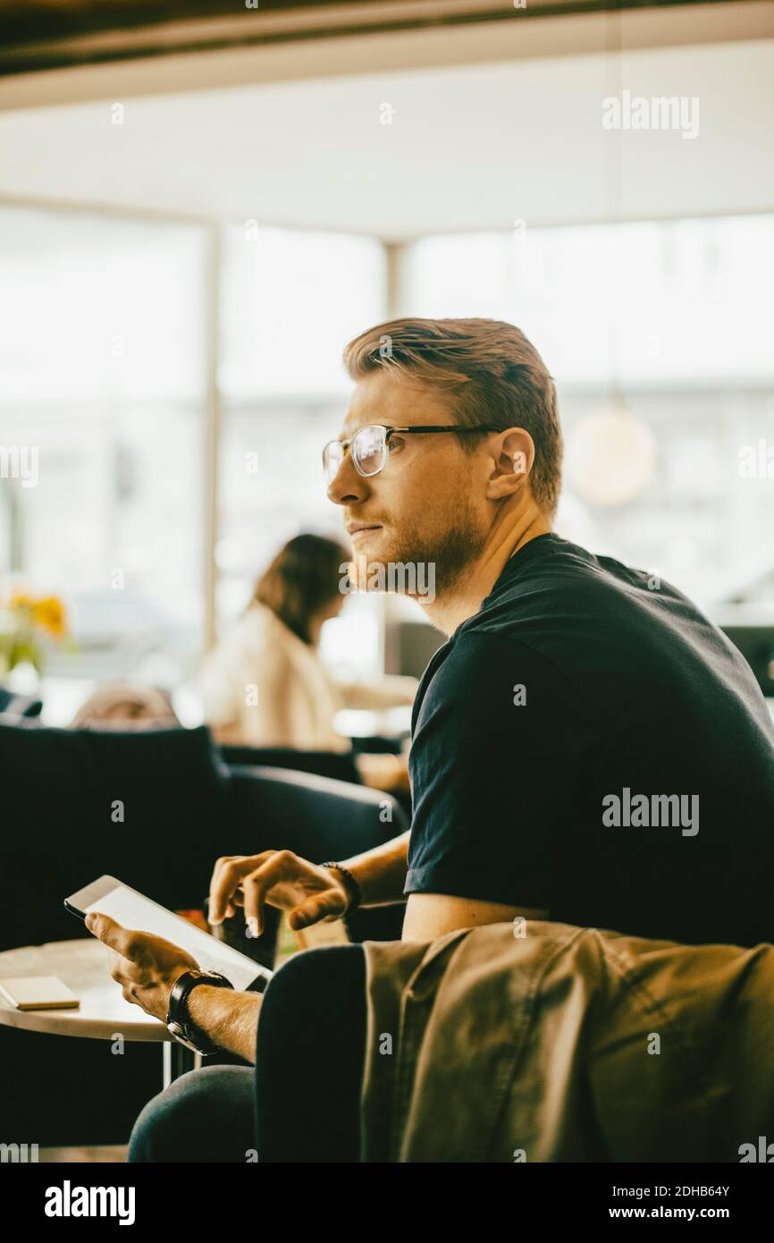 Mid adult man using digital tablet while looking away in restaurant Stock Photo