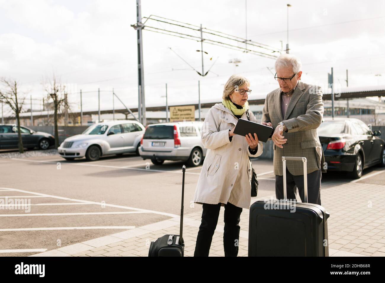 Senior Couple Using Digital Tablet While Standing With Luggage At Parking Lot Against Sky Stock Photo Alamy