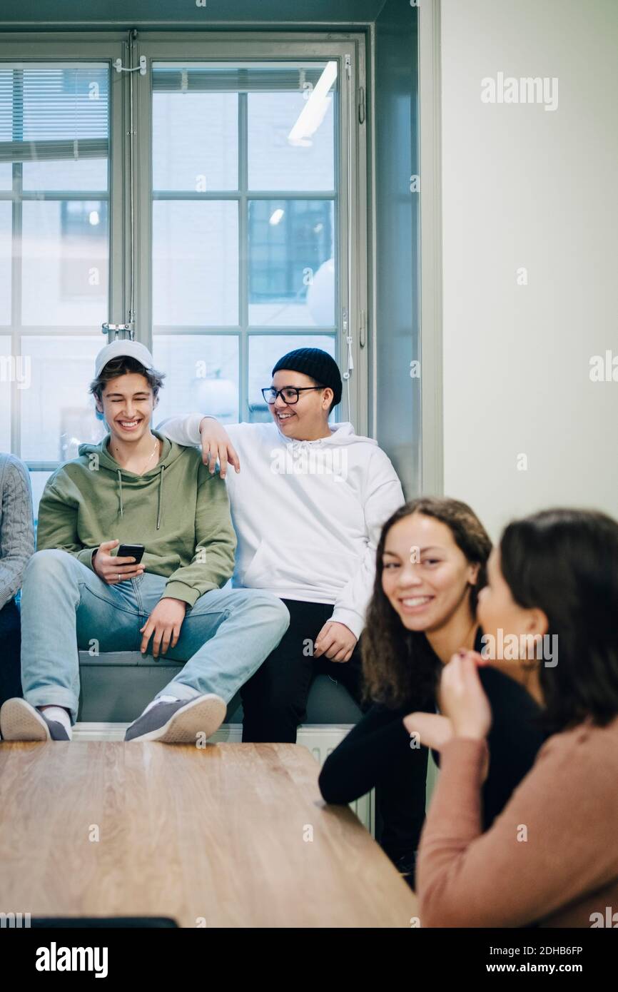 Smiling teenage students talking while sitting classroom Stock Photo ...