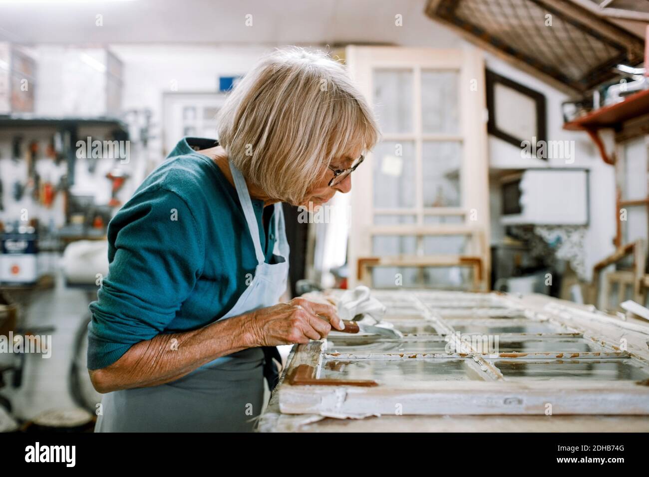 Side view of senior female owner scraping window frame on workbench at ...
