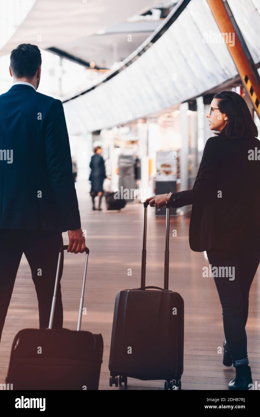 Rear view of business couple with luggage walking in airport terminal ...
