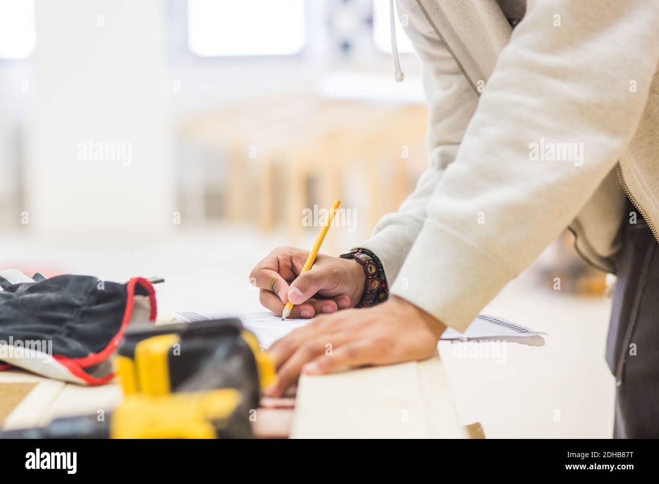 Midsection of male teenage carpenter drawing diagram on paper at workbench in workshop Stock Photo