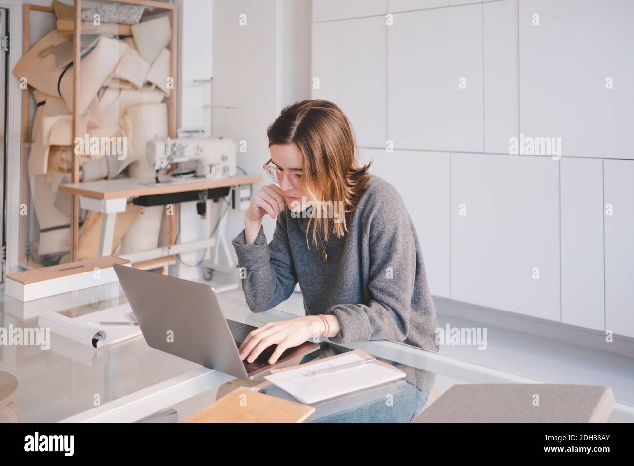 Young female fashion designer using laptop at desk in store Stock Photo