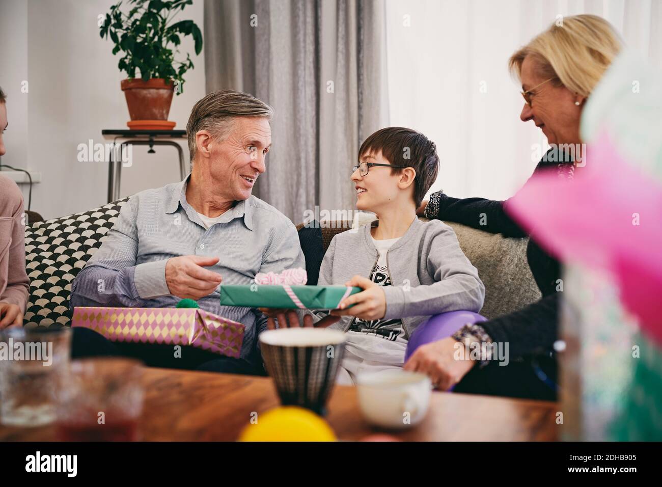 Happy grandfather receiving gifts from grandson at birthday party Stock