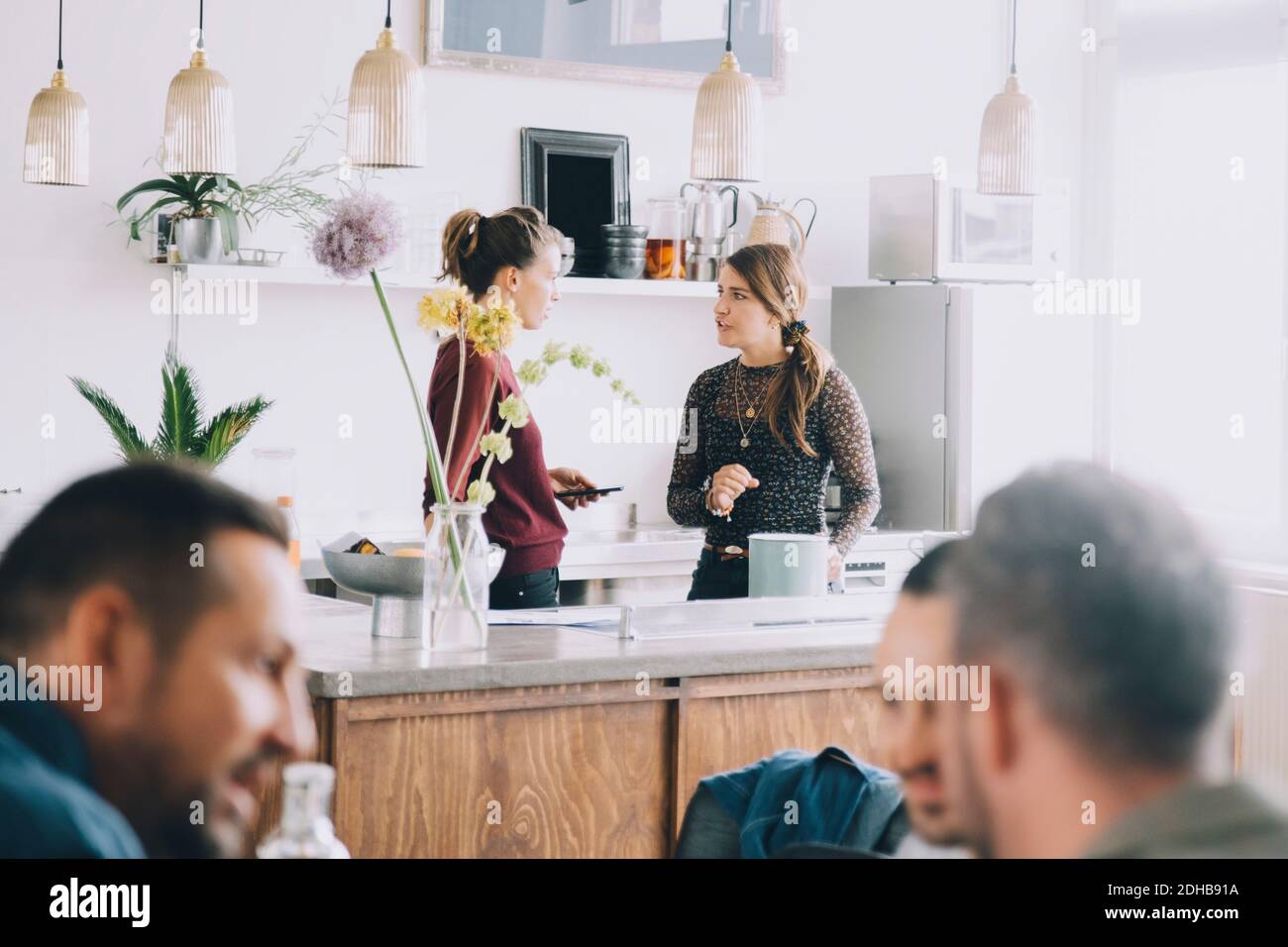 Creative female entrepreneurs discussing at kitchen island while colleagues in foreground at office Stock Photo