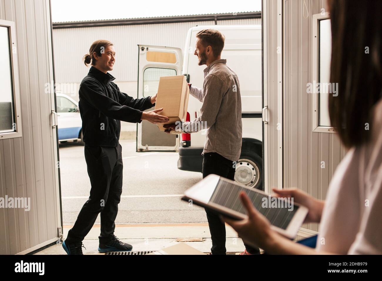 Female using digital tablet while male coworkers delivering boxes in van Stock Photo